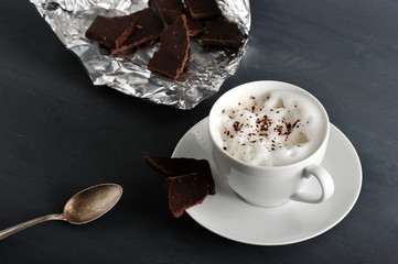 A cup of coffee. On a saucer bitter chocolate. Milk foam on coffee is sprinkled with crumbs of...