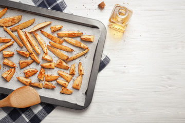 Baking sheet with delicious oven baked potatoes on table