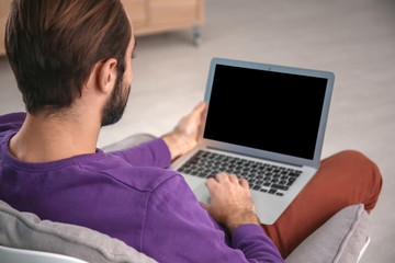 Man with laptop sitting in comfortable armchair at home