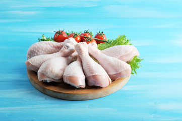 On a round wooden tray, raw chicken legs. Chicken legs are located in a semicircle on lettuce...