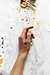 Overhead view of female artist hands soiled with golden and violet paints on white background. Artist workspace concept.