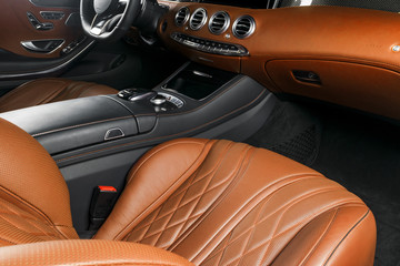 Modern Luxury car inside. Interior of prestige modern car. Comfortable leather seats. Orange perforated leather cockpit. Steering wheel and dashboard. automatic gear stick shift. Car interior details