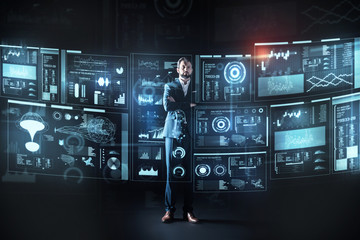 Obraz premium Serious person. Clever attentive calm programmer feeling confident while standing in front of a giant futuristic screen with his arms crossed and thoughtfully looking at the new information