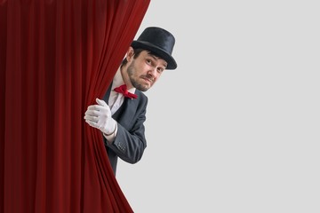Nervous actor or illusionist is hiding behind red curtain in theater.