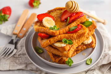 French toasts with honey, banana and strawberries on gray plate. Gray background