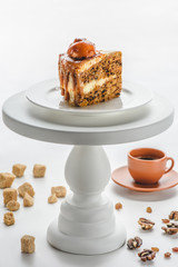 piece of delicious caramel cake on white cake stand, coffee on table