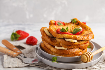 French toasts with honey, banana and strawberries on gray plate. Gray background
