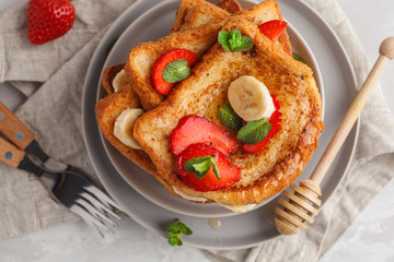 French toasts with honey, banana and strawberries on gray plate. Gray background, copy space, top view.