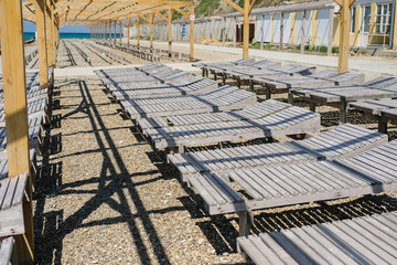 Close-up wooden sun loungers on a pebbled public beach by the sea. Side view