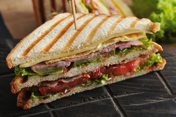 Half of a sandwich in the form of a triangle on a wooden board. The filling consists of ham,...