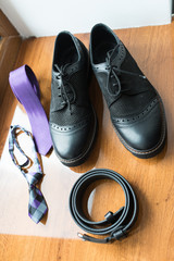 Fototapeta na wymiar The groom's and a dog’s wedding accessories. Lilac neck tie and a black leather belt and black shoes on a wooden background.