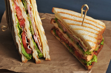Club sandwich with bacon and ham on kraft paper. The sandwich is divided in half into two triangles. The sandwich is made from white bread, fried on a grill. Close-up. Macro photography.