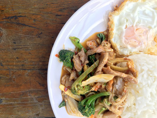 Asian style stir-fry meat slices with fresh vegetable with rice and fried eggs in thai style placed on white dish on wooden table.