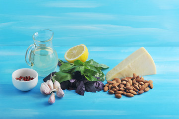 Ingredients for green pesto sauce. In the frame, green basil, almonds, garlic, half a lemon, a jug of olive oil, spices  and parmesan cheese. Blue wood background. Close-up.