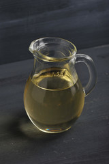 On a dark wooden background a glass jug with olive oil. Close-up. Macro photography. Vertical orientation of the picture.