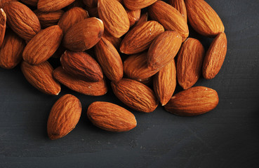 On a dark wooden surface there are almonds. Almonds are an excellent antioxidant. Nuts are widely used in cooking. View from above. Close-up. Macro photography.