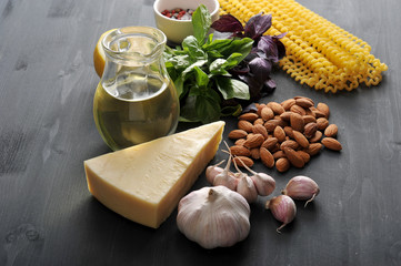 Ingredients for pasta with pesto sauce. In the frame, green and purple basil, almonds, parmesan cheese, garlic, spices, olive oil and Fusilli lunghi pasta. Dark background. Close-up. Vertical shot.