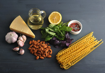 Ingredients for pasta with pesto sauce. In the frame, green and purple basil, almonds, lemon, parmesan cheese, garlic, spices, olive oil and Fusilli lunghi bucati pasta. Dark background. Close-up.