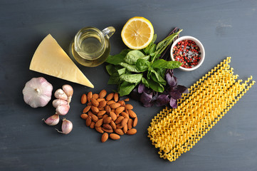 Ingredients for pasta with pesto sauce. In the frame, green and purple basil, almonds, half a lemon, parmesan cheese, garlic, spices, olive oil and pasta Fusilli lunghi. Close-up. View from above.