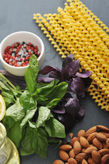 Everything you need for cooking pasta with pesto sauce. In the frame, green and purple basil, almonds, parmesan cheese, lemon, spices, olive oil and Fusilli lunghi pasta. Dark background. Close-up.