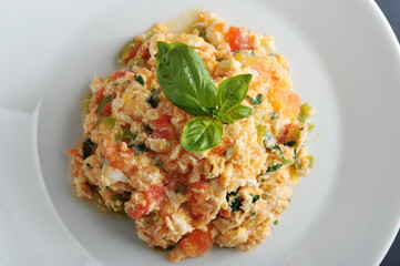 Traditional Turkish fried eggs with tomatoes (menemen). Also called an omelette with vegetables. The dish is decorated with fresh basil leaves. View from above. Close-up. Macro photography. 