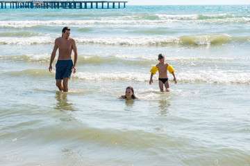 Mum, son and dad splashong and swimming in sea waves. Boy in water wings.