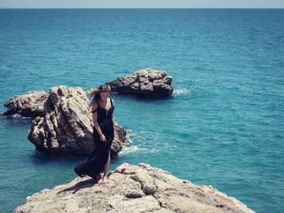 Fototapeta na wymiar Young woman in black dress on the rocks