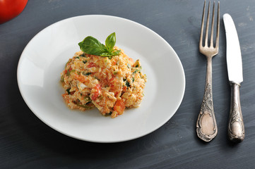 Traditional Turkish fried eggs with tomatoes (menemen). Also called an omelette with vegetables. The dish is decorated with fresh basil leaves.  There are cutlery nearby. Close-up. Macro photography.