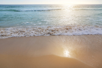 Surf wave is covering a sea beach sand with sunset light.
