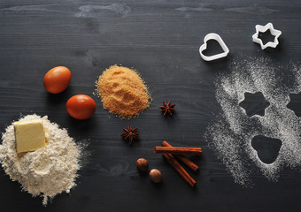Ingredients for the preparation of home made shortbread cookies: eggs, flour, butter, cane sugar, cinnamon sticks, anise, nutmeg. Next form for the cookie. Dark wooden background. View from above.