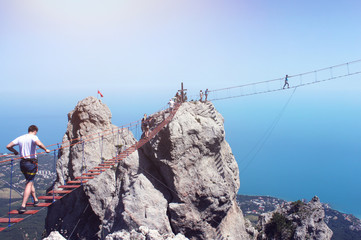 Obraz premium Tourists go on a cable car on the bridge, on top of the mountain ai-petri, against the background of the sea.