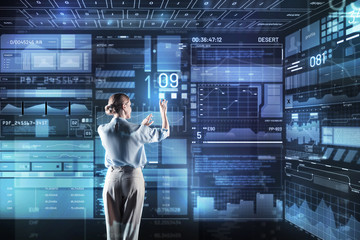 Fototapeta premium Convenient device. Clever qualified young programmer feeling confident while standing in her modern office and working with a giant futuristic transparent device