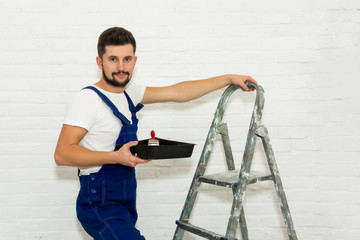 Young man with dark hair is painting the wall in white in his apartment.