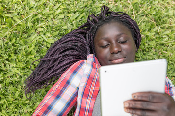 African teenager using tablet laying on the grass