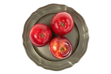 Trzy dorodne, czerwone jabłka na metalowym talerzu, centralnie z góry na białym tle