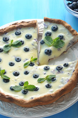 Tart with white chocolate and blueberries. Blue wood background. Vertical orientation of the frame. View from above. Close-up. Macro photography.