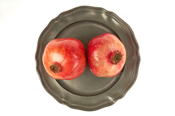 Dwa dorodne owoce granata na metalowym talerzu, centralnie z góry na białym tle