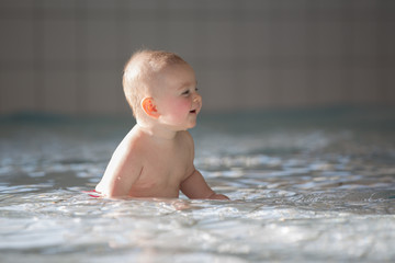 Little cute baby boy, swimming happily in a shallow pool water