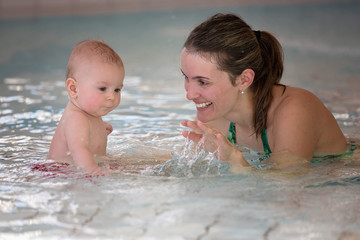 Little cute baby boy, swimming happily in a shallow pool water