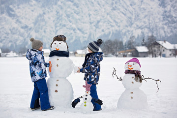 Family with children, building snowman in the park in little village in Austria
