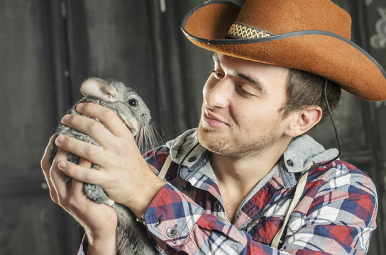 Portrait of a Cowboy. dark hair, jeans , plaid shirt. he holds the chinchilla animal