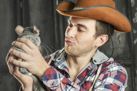 Portrait of a Cowboy. dark hair, jeans , plaid shirt. he holds the chinchilla animal