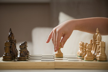 Child's hand holding chess figure while playing chess. Little clever child playing chess at home....