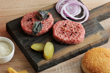 On a wooden board, two hamburger cutlets, cucumber slices marinated, onion rings red. On one of the cutlets is a basil leaf. Close-up. Macro photography.