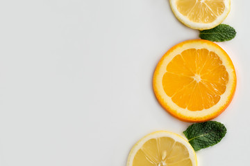close-up slices of lemon, orange and mint leaves laid out on a white homogeneous background