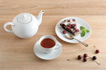 Portion of chocolate brownies on a plate. The pie is decorated with a mint leaf. Next cup with tea and a teapot. Fresh cherries are on the table. Serving for one person. Light wooden background.