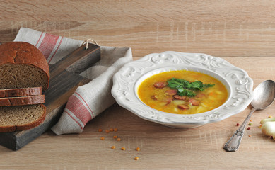 Pea soup with smoked sausages and parsley. Next to the plate is a spoon and bread on a cutting...