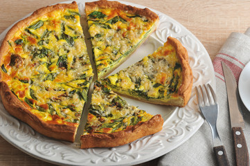 Open pie of quiche with spinach on a white plate. View from above.