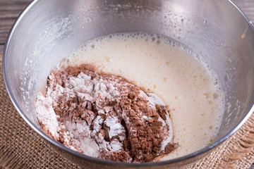 Preparing a dough/batter for crepes or pancakes with wheat flour and cocoa in bowl, milk, eggs and oil