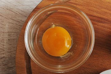 Raw chicken egg without shell in a glass bowl. A bowl on a wooden tray. View from above. Closeup.